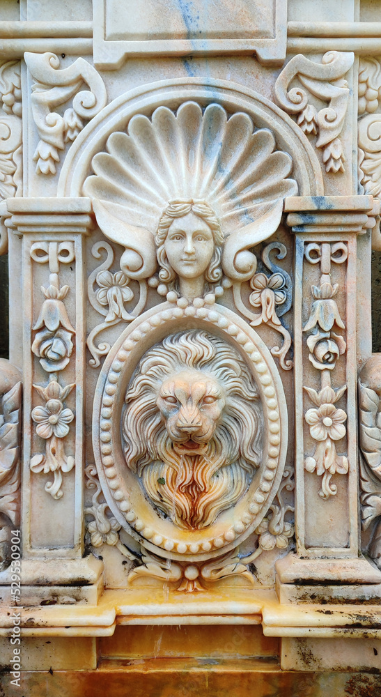 ancient white marble fountain decorated with the head of a lion and of a woman, with palace ornaments from a fairy tale with ancient texture - vertical image