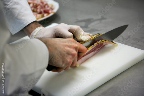 Uomo che taglia una fetta di pancetta, mani e coltello in primo piano photo