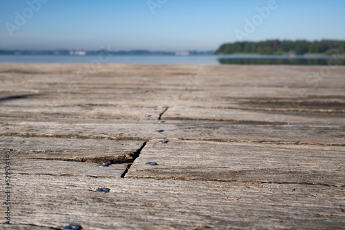 Old pier made of wooden weathered boards with nails, against the backdrop of a lake and a blue sky, on a summer sunny day. 