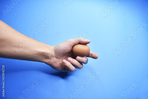 Man's hand holding egg on blue background.