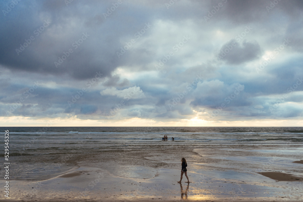 person walking on the sandy Atlantic Ocean Beach during the cloudy sunset 