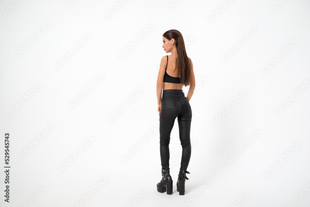 a brunette girl with long hair in black leather pants and boots poses on a white background.youth fashion. a brunette girl with long hair in black leather pants and boots poses on a white background.youth fashion.