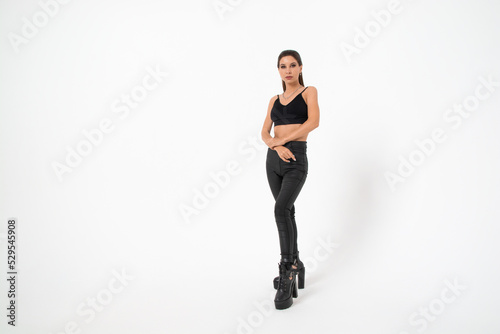 a brunette girl with long hair in black leather pants and boots poses on a white background.youth fashion.