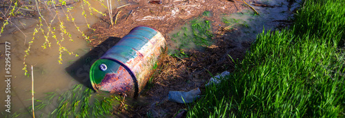 Water pollution caused by barrel with toxic waste dumped into the river along with plastic bottles and other garbage