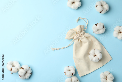 Cotton eco bag and flowers on light blue background, flat lay. Space for text