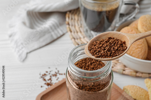 Spoon of instant coffee over jar on white table, closeup. Space for text