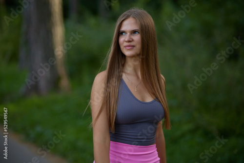 Lovely young woman with sexy boobs in trendy gray top in pink fashionable sports shorts walking on street. Pretty beauty girl fashion model walks in park. Healthy lifestyle. 