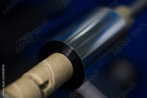 TTR ribbon on shaft of winding machine in the printing house. Black roll wax ribbon for thermal transfer for a special barcode printer. Consumables materials for barcode printing. Selective focus