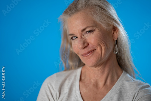 Portrait of happy smiling flirty mature woman isolated on blue background studio. People lifestyle concept