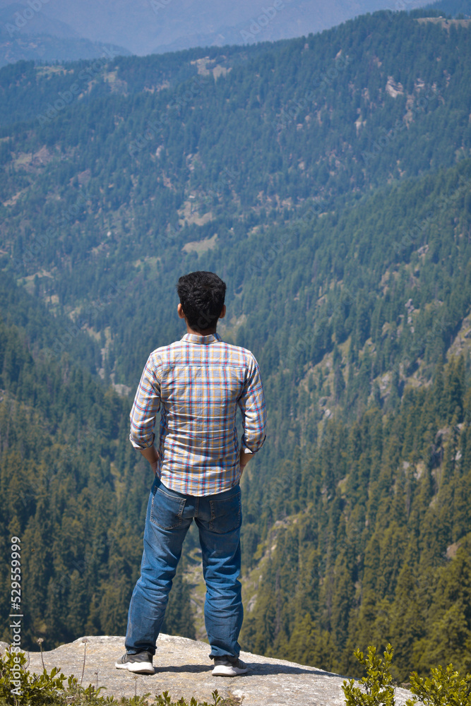Naklejka premium Man standing on cliff back towards camera. Mountain valley in background