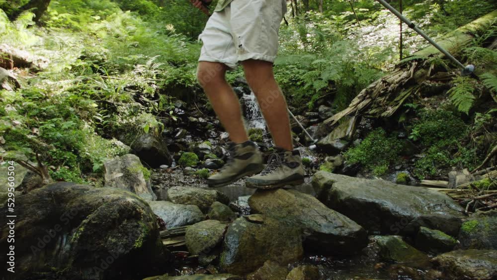 Tourist in sports trekking shoes crosses spring stream on stones. Sports shoes do not slip on wet stones. Trekking boots are key to healthy feet on hike