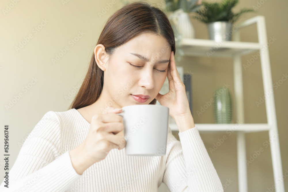 Suffer, attractive asian young woman, girl holding mug, cup of coffee, having headache, migraine after drinking strong caffeine or tea while working from home, face expression stress, illness people Suffer, attractive asian young woman, girl holding mug, cup of coffee, having headache, migraine after drinking strong caffeine or tea while working from home, face expression stress, illness people
