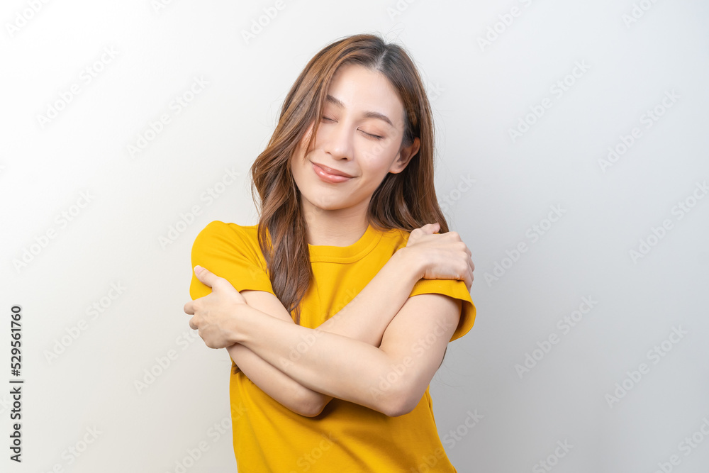 Smiling positive, hugging oneself happy asian young woman wearing yellow casual, portrait of beautiful brunette with long hair, self love and self care, expression hug standing isolated on background. Smiling positive, hugging oneself happy asian young woman wearing yellow casual, portrait of beautiful brunette with long hair, self love and self care, expression hug standing isolated on background.