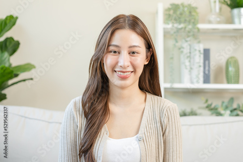 Smiling positive, attractive asian young woman wearing casual dress, portrait of beautiful brunette her with long brown hair, feeling happy looking to camera sitting on sofa, isolated on background.