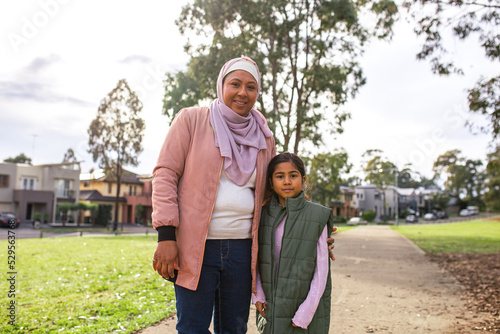 Smiling middle aged woman wearing pink hijab with a girl wearing green coat on a path way photo