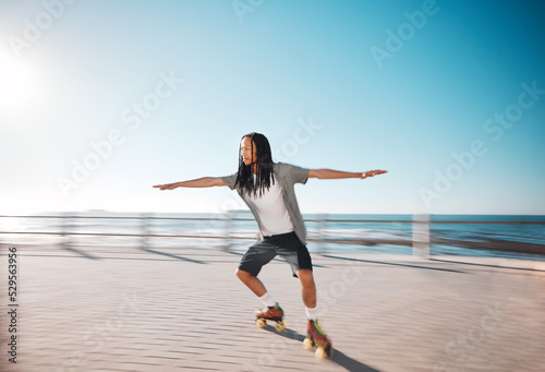Man roller skating on the promenade at the beach during a summer holiday for fun and exercise. Young, fit and healthy guy skating for a fitness workout on boardwalk in nature by the ocean on vacation