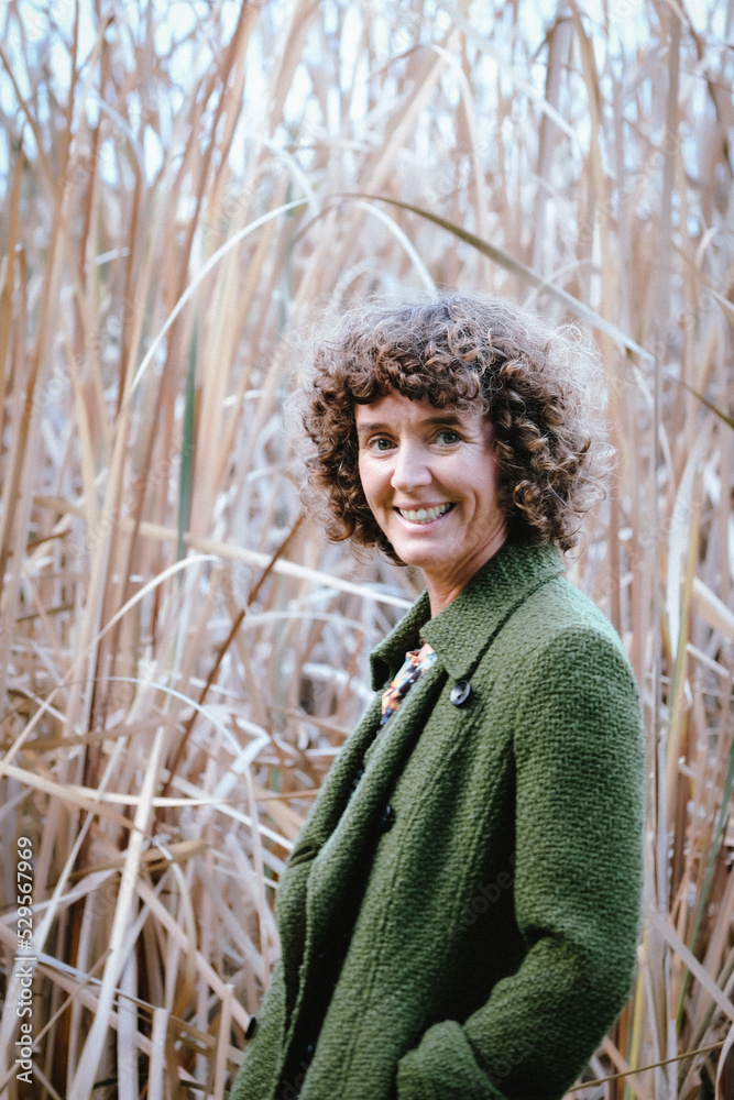 Woman with curly hair posing in front of bushland and reeds grass ...
