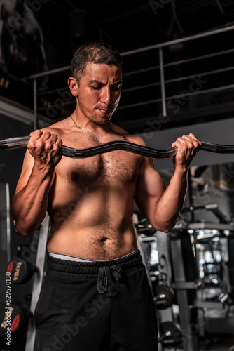 High quality photography. A muscular man training with a barbell. Latin man making a lot of effort when lifting a barbell with weight. A shirtless man in the gym.