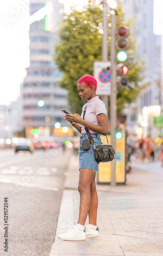 Afro young woman standing on the street using the mobile
