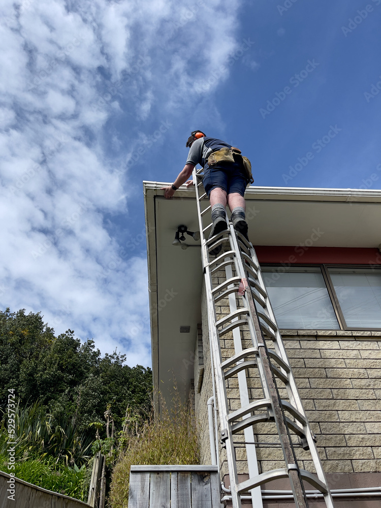 Young caucasian man in his 30's working to replace a section of plastic guttering on a 1970's house in New Zealand