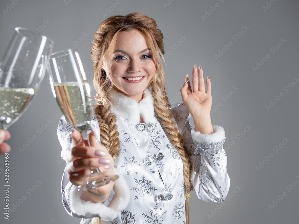 New Year's toast, a young beautiful blonde in a snow queen costume clinks a glass of champagne, photo on gray, copy space New Year's toast, a young beautiful blonde in a snow queen costume clinks a glass of champagne, photo on gray, copy space