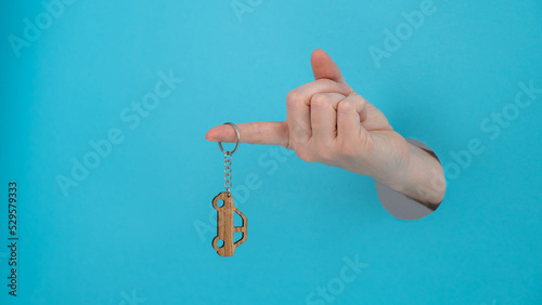 Woman's hand holding a wooden keychain in the shape of a car on a blue background.