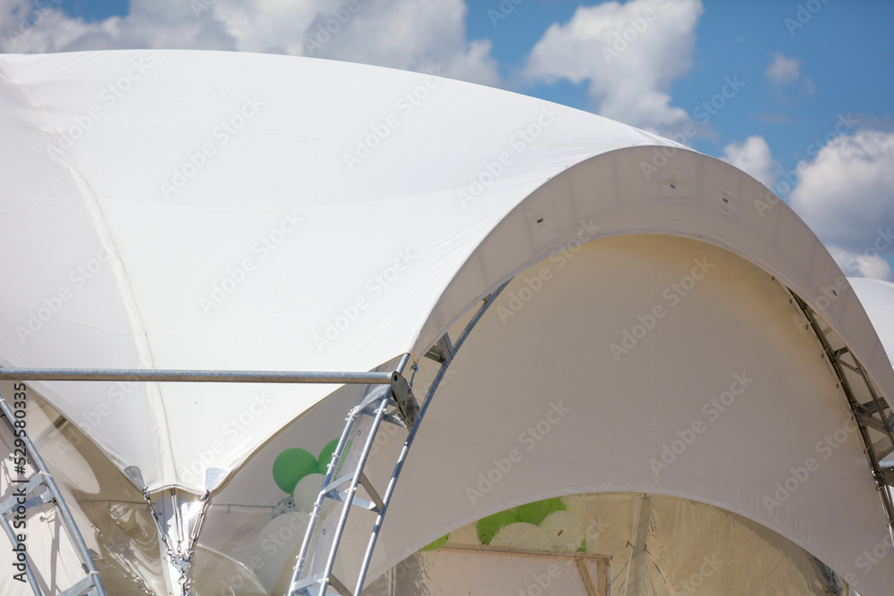Construction of a large white tent against the sky.