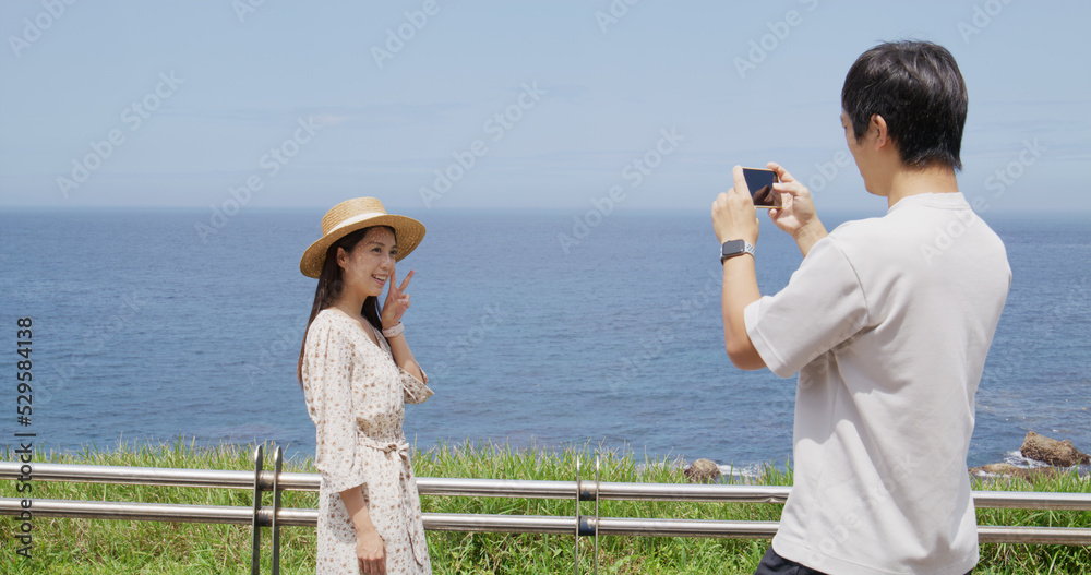 Man help his wife to take photo on cellphone beside the sea Man help his wife to take photo on cellphone beside the sea