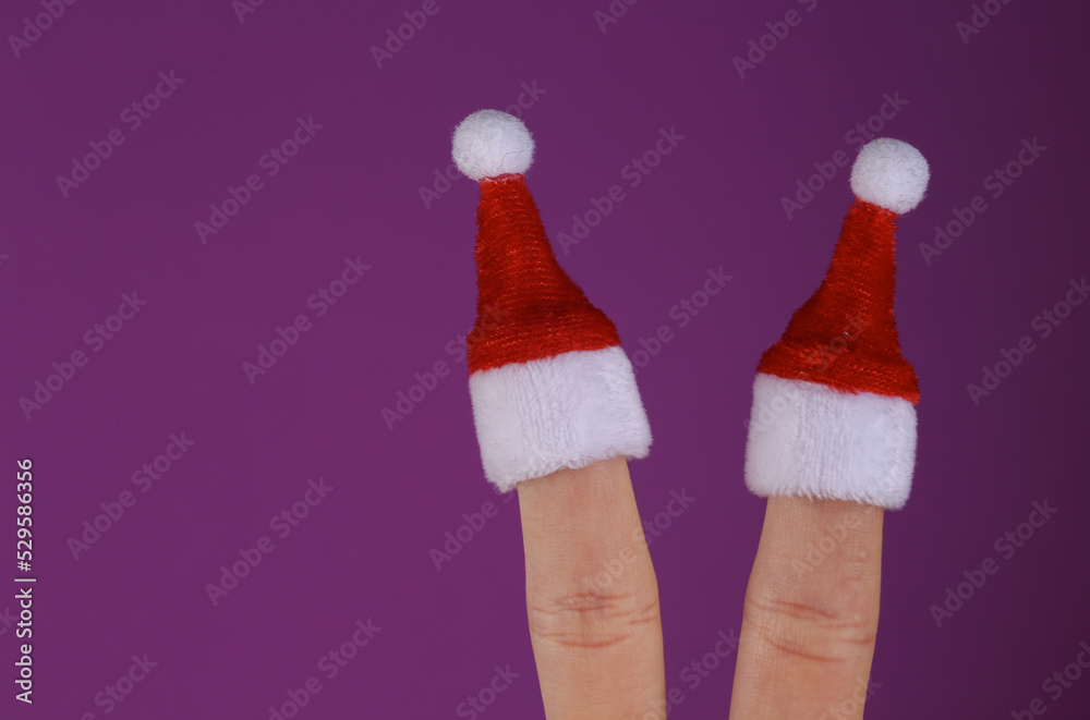 Mini Santa hats on the fingers of female hand on purple background. Christmas concept Mini Santa hats on the fingers of female hand on purple background. Christmas concept