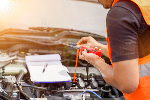 Closeup and crop motor vehicle mechanic checking engine oil to record the repair history with sun and lens flare background.