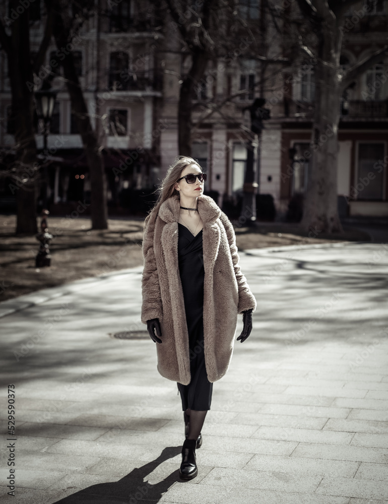 Fototapeta premium Fashion woman in warm fur coat, gloves and sunglasses walking in city
