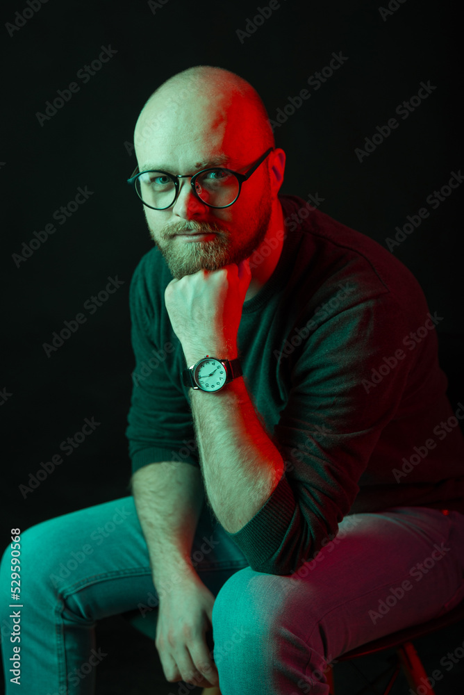 Vertical portrait of a man sitting and looking at the camera in a dark room. Vertical portrait of a man sitting and looking at the camera in a dark room.