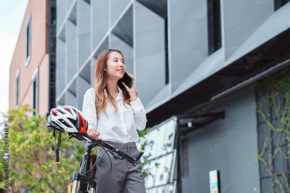 Asian businesswoman use smart mobile phone during go to office work at city street with bicycle, Happy female commuting outside in morning, Eco friendly people lifestyle concept.