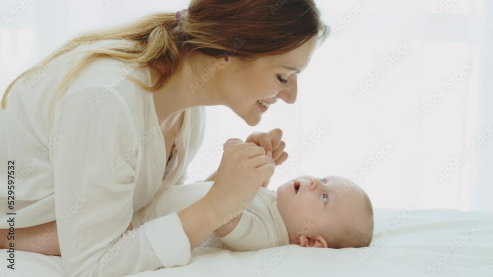 Young caucasian mother having fun and kiss with newborn baby in cozy kids bedroom. Caring mom and neonate toddler together at home. Concept of childhood, motherhood and new life Young caucasian mother having fun and kiss with newborn baby in cozy kids bedroom. Caring mom and neonate toddler together at home. Concept of childhood, motherhood and new life