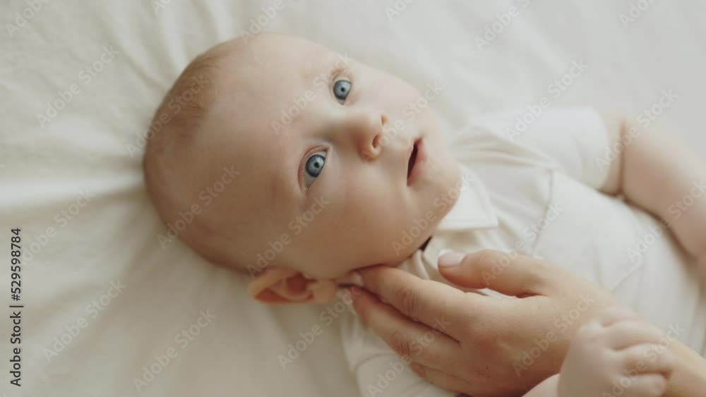 Beautiful newborn baby lying on the bed and mother hand stroking his face. Little boy lying and enjoying while mother stroking his face. Concept of childhood, motherhood and new life Beautiful newborn baby lying on the bed and mother hand stroking his face. Little boy lying and enjoying while mother stroking his face. Concept of childhood, motherhood and new life