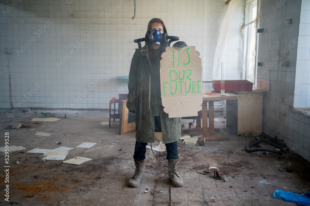 Environmental pollution, ecological disaster, nuclear war, woman in gas mask with a banner that says: it's our future. Post apocalypse. Face-guard to prevent breathing toxic air. Environmental pollution, ecological disaster, nuclear war, woman in gas mask with a banner that says: it's our future. Post apocalypse. Face-guard to prevent breathing toxic air.