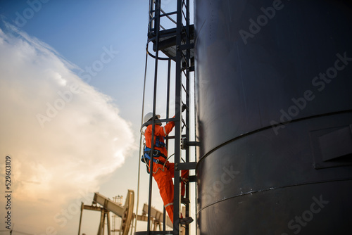 Foto man working in Oil rig or Oil field site, climb oil tank for working in evening time with surrise or sunset