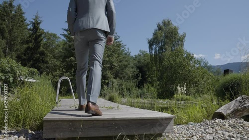 Mann im Anzug geht über den Holzsteg am Teich photo