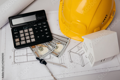 Top view of construction drawings, safety hat, calculator and house model on a table