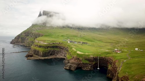 Aerial view of Mulafossur waterfall, Faroe Islands. Small village Gasadalur with a Hvannadalur valley and Arnafjall mountain hidden in a fog. Sunny day in summer. High quality 4k footage. photo