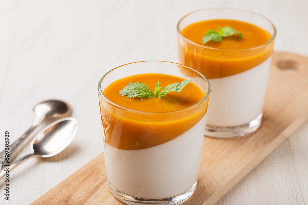 Vegan dairy free coconut Panna cotta with mango sauce in glasses on white wooden table. Healthy vegan dessert. Vegan dairy free coconut Panna cotta with mango sauce in glasses on white wooden table. Healthy vegan dessert.