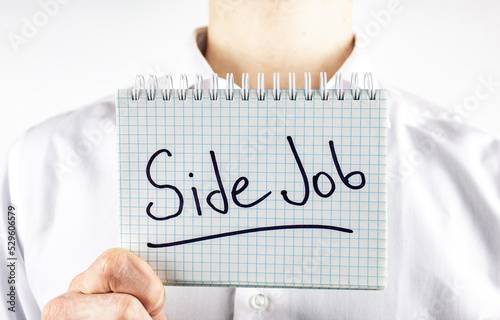 A man holds a notepad with the inscription side job. The concept of part-time work, remote work, freelance, job search.