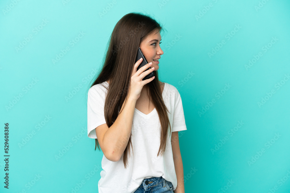 Young caucasian woman isolated on blue background keeping a conversation with the mobile phone with someone Young caucasian woman isolated on blue background keeping a conversation with the mobile phone with someone