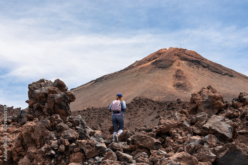 Woman with backpack on volcanic desert terrain. Hiking trail leading to summit volcano Pico del Teide, Mount Teide National Park, Tenerife, Canary Islands, Spain, Europe. Solidified lava, ash, pumice
