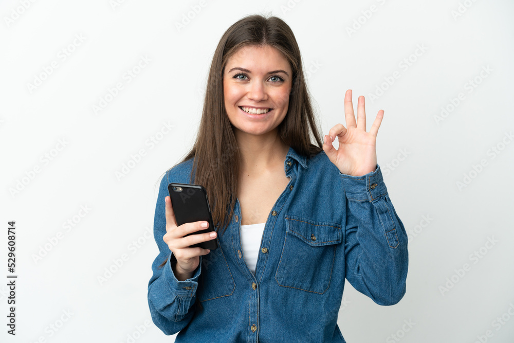 Young caucasian woman isolated on white background using mobile phone and doing OK sign Young caucasian woman isolated on white background using mobile phone and doing OK sign