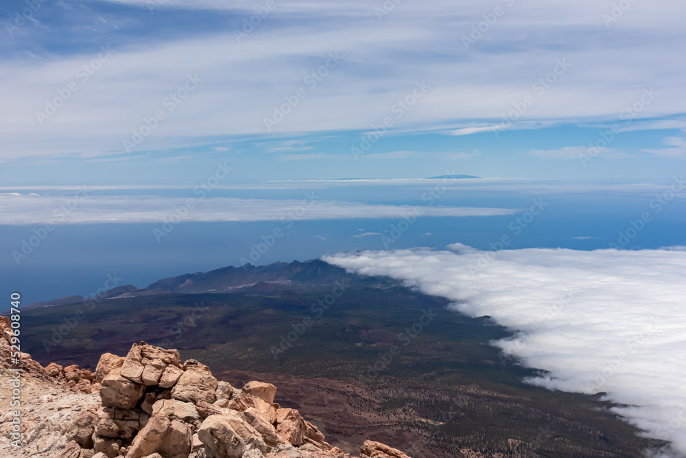 Scenic view from summit of volcano Pico del Teide over the island of Tenerife, Canary Islands, Spain, Europe. Vista on barren landscape, solidified lava, ash, pumice. Valley and sea covered in clouds