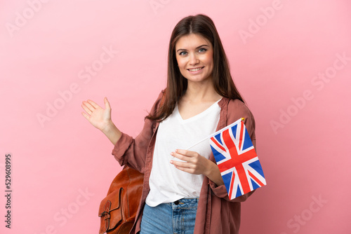 Young caucasian woman holding an United Kingdom flag isolated on pink background extending hands to the side for inviting to come