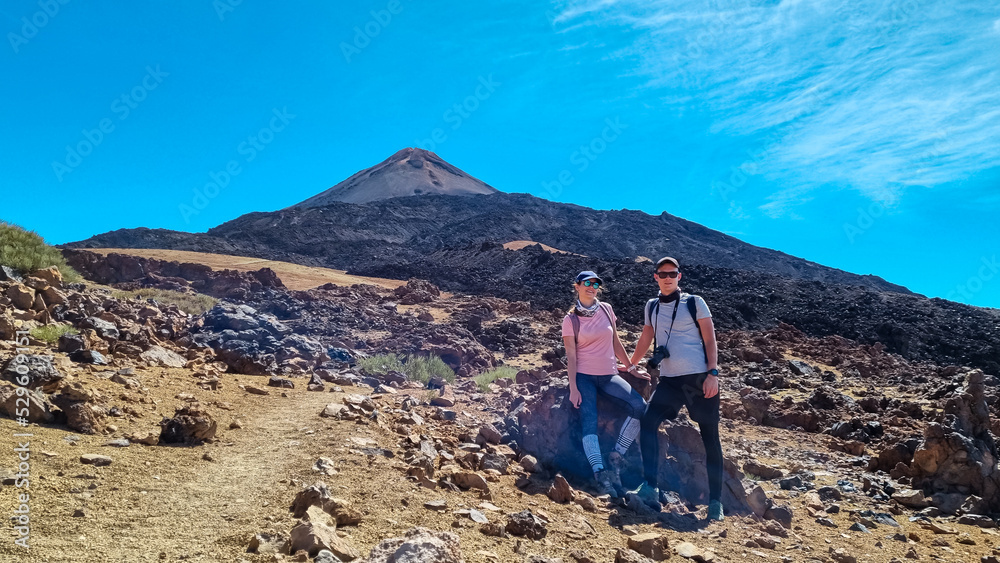 Front view of couple with backpacks on volcanic desert terrain hiking trail leading to summit volcano Pico del Teide, Teide National Park, Tenerife, Canary Islands, Spain, Europe. Solidified lava, ash