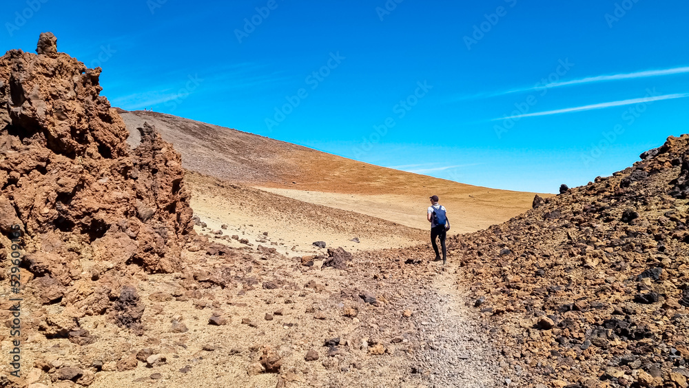 Man with backpack on volcanic desert terrain hiking trail leading to summit volcano Pico del Teide, Mount Teide National Park, Tenerife, Canary Islands, Spain, Europe. Solidified lava, ash, pumice