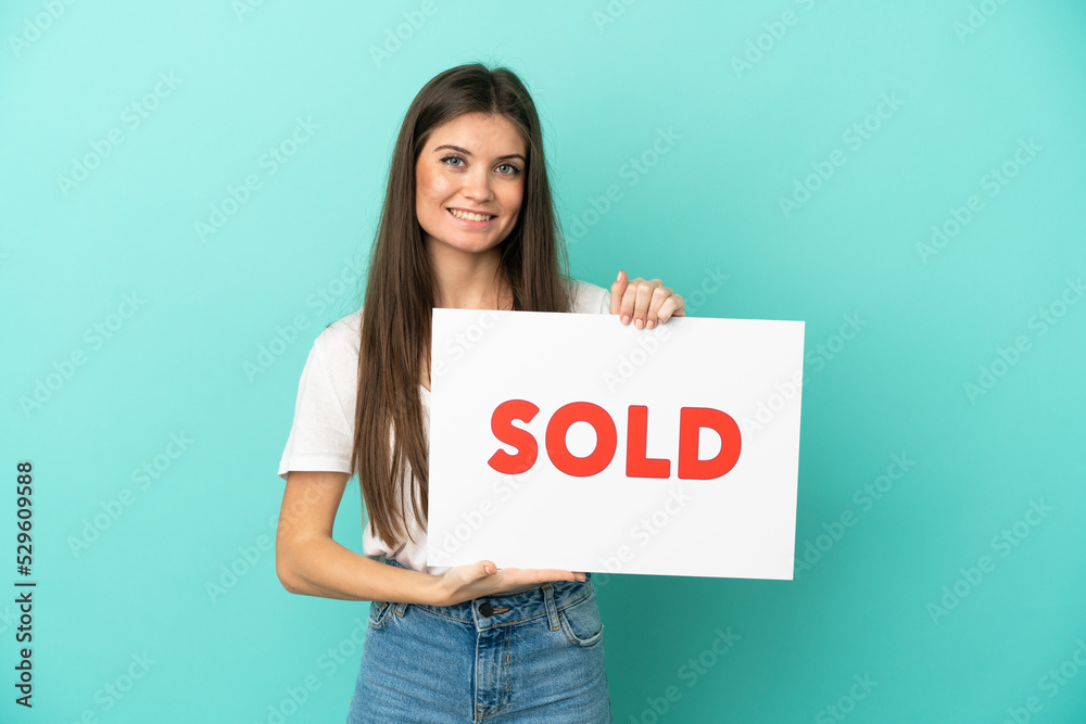 Young caucasian woman isolated on blue background holding a placard with text SOLD with happy expression Young caucasian woman isolated on blue background holding a placard with text SOLD with happy expression